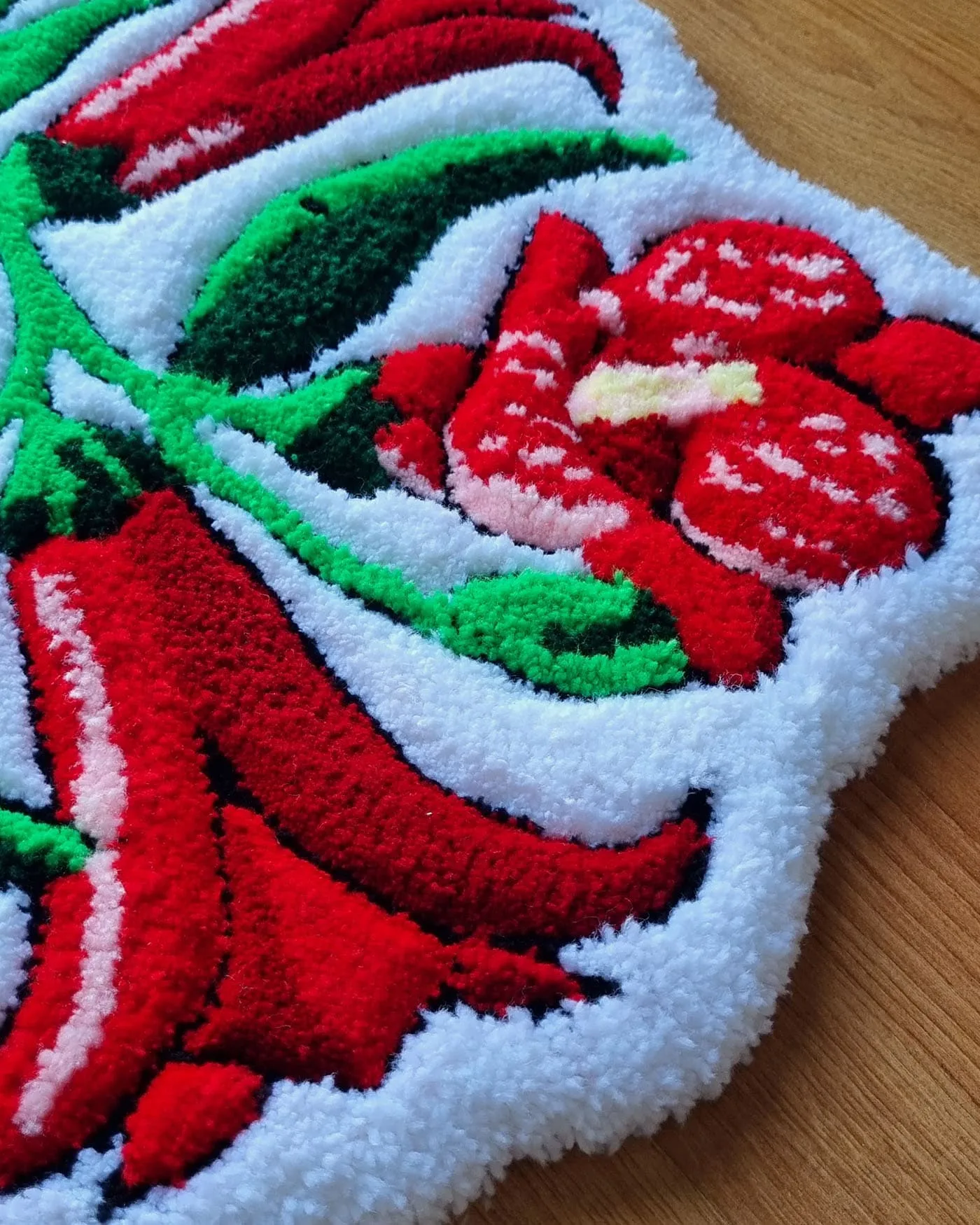 Detalle de diseño floral copihue mostrando pétalos rojos y tallo verde sobre alfombra tejida.