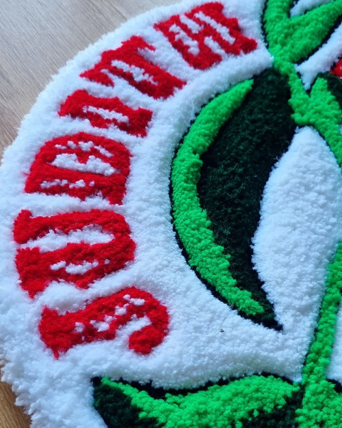 Detalle de la alfombra Flor Copihue con inscripción tejida a mano y fondo blanco suave.