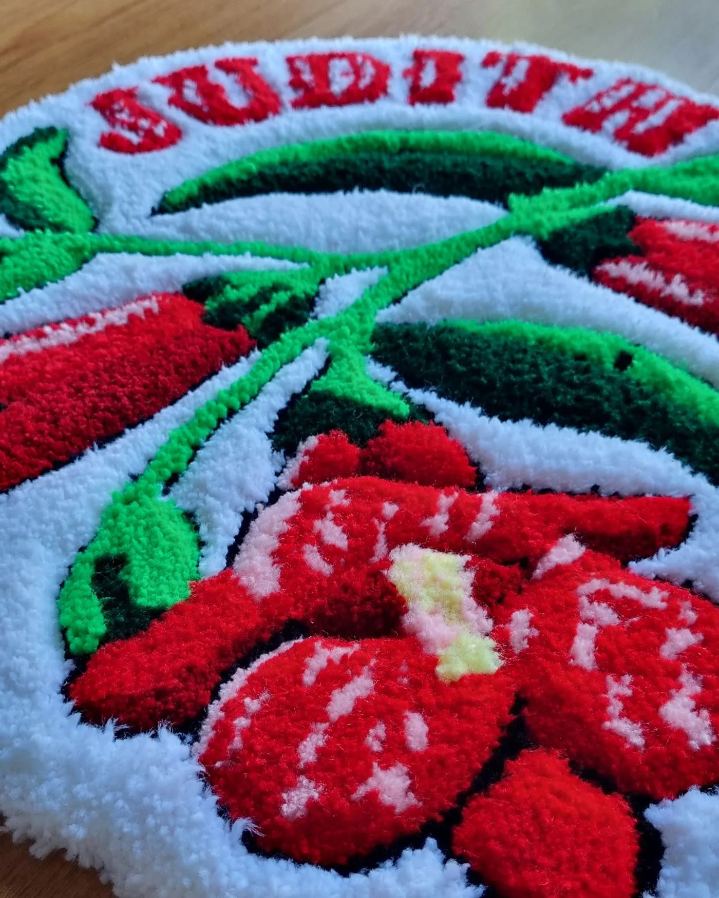 Plano lateral de alfombra flor copihue roja con pétalos definidos y textura de lana artesanal.
