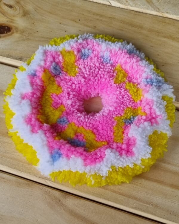 Alfombrita posavasos en forma de donut vista en ángulo lateral, con bordes suaves y diseño colorido.